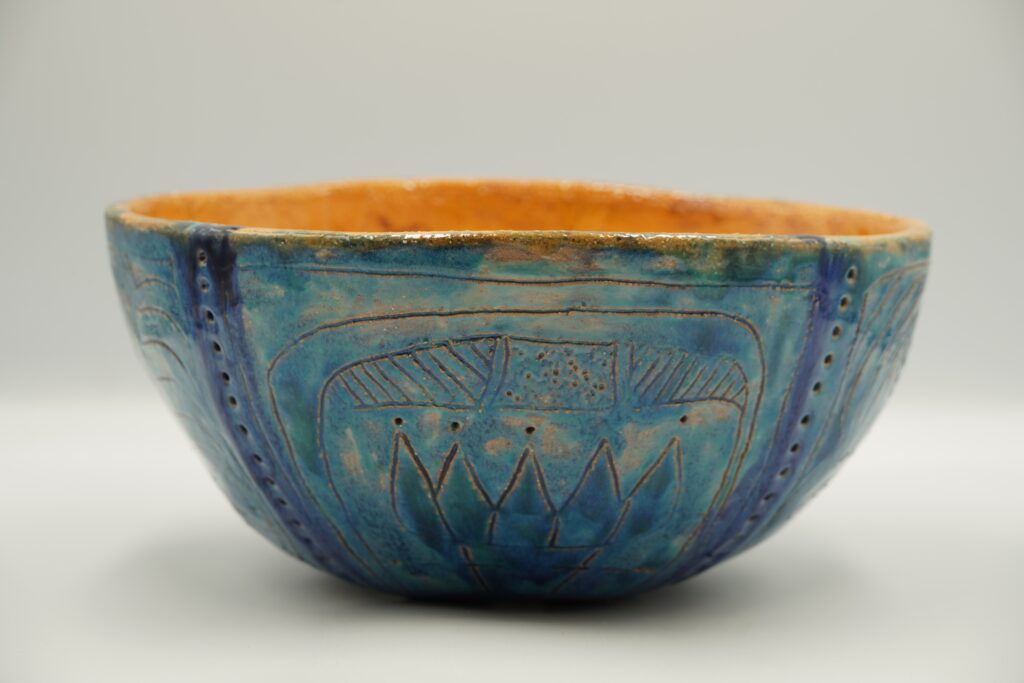 Taça de cerâmica artesanal azul com motivos gravados e interior alaranjado